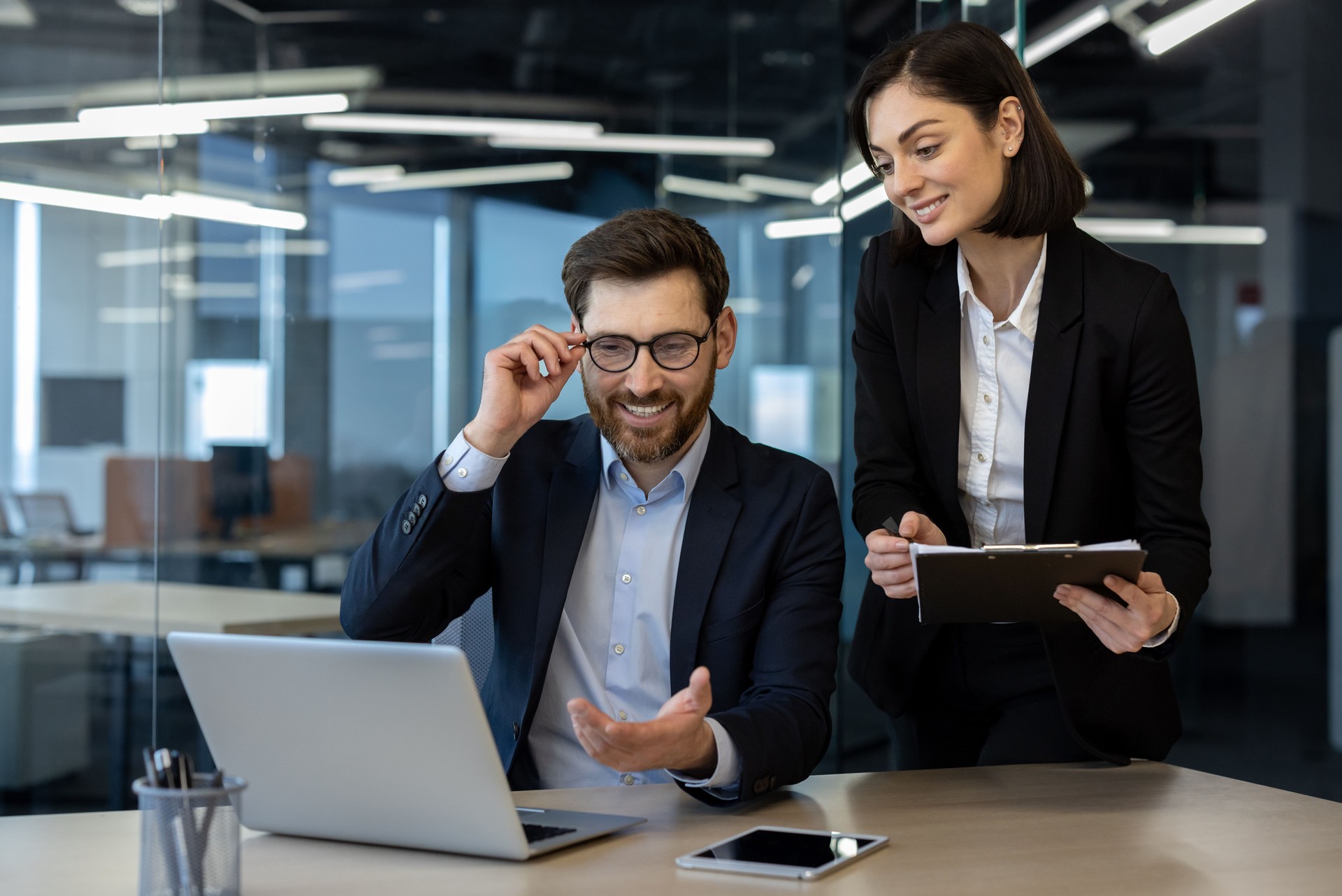 Smiling businessman engaging in lively discussion with colleague in modern office setting with laptop and phone